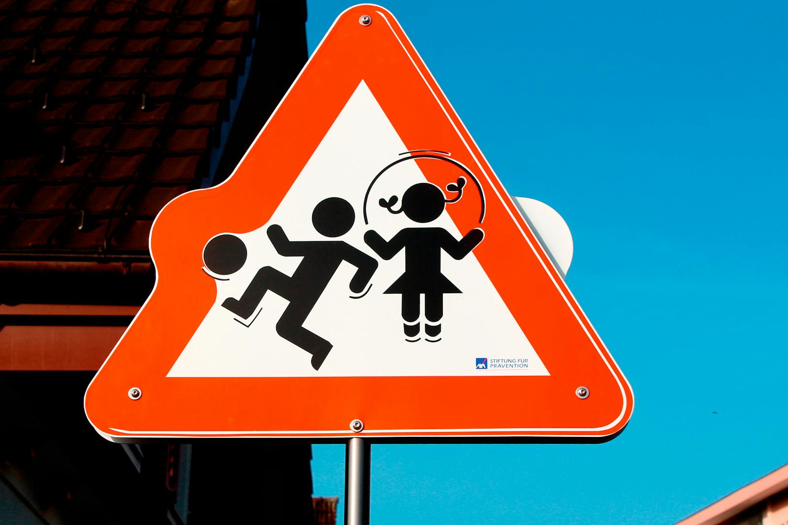 Triangular road sign depicting children playing, emphasizing safety against a bright blue sky.